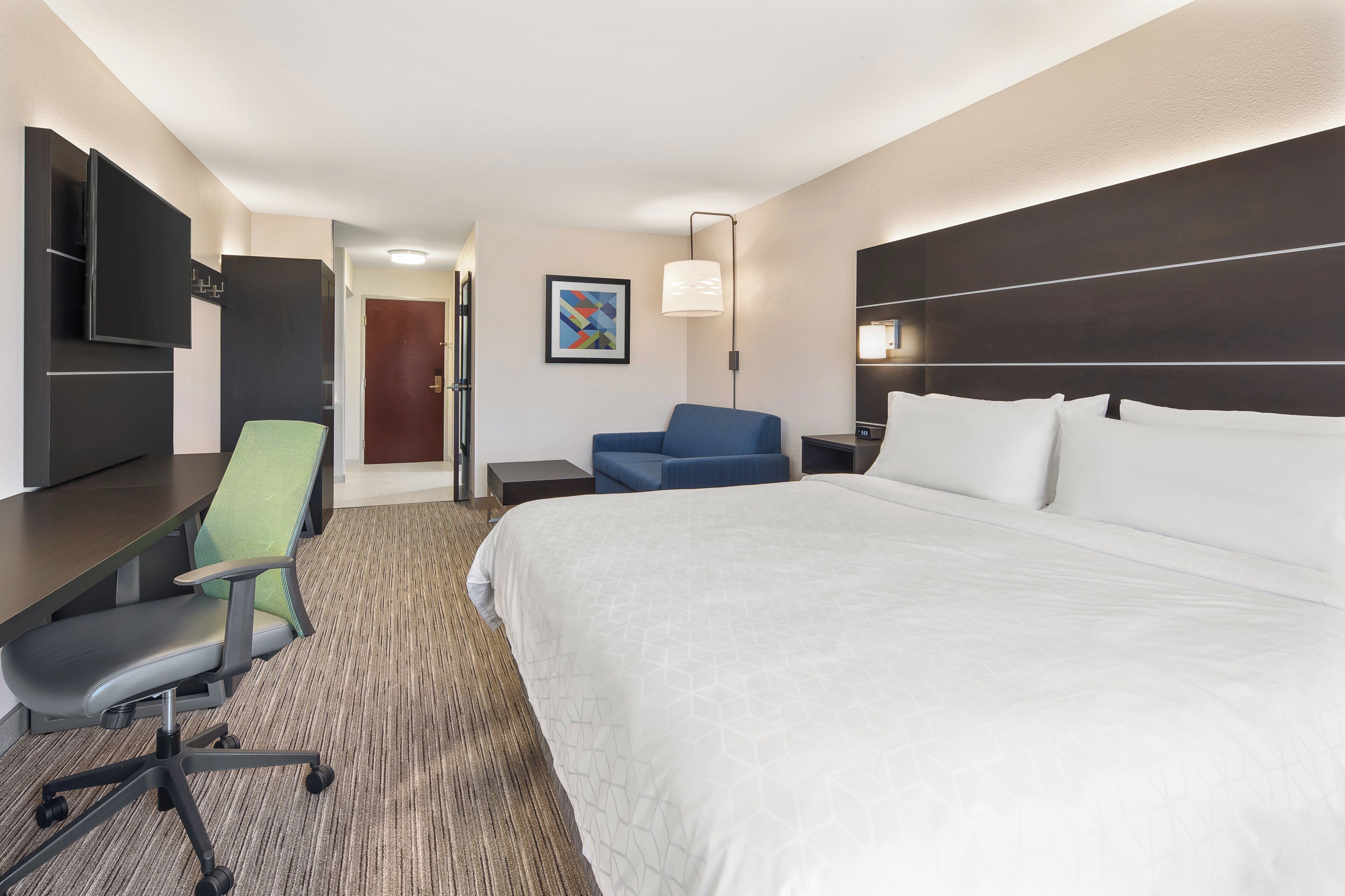 A hotel room with a bed, a desk, a chair, a TV, and a painting on the wall.