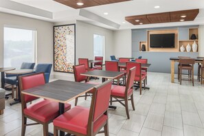 A hotel dining area with multiple tables and chairs, a large window, and a flat-screen TV mounted on the wall. - Holiday Inn Express & Suites Greenville-Spartanburg (Duncan) by IHG (Duncan)