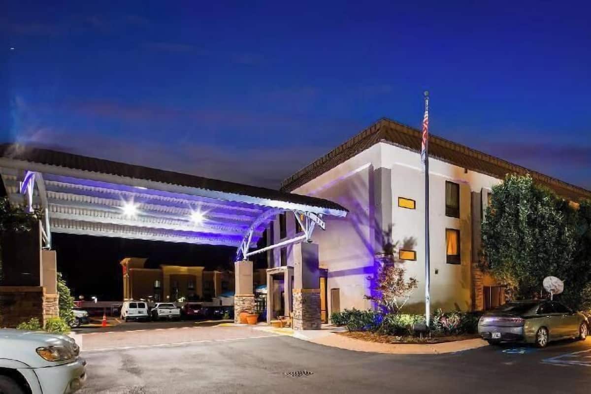 Un hotel con entrada techada, asta de bandera y estacionamiento.