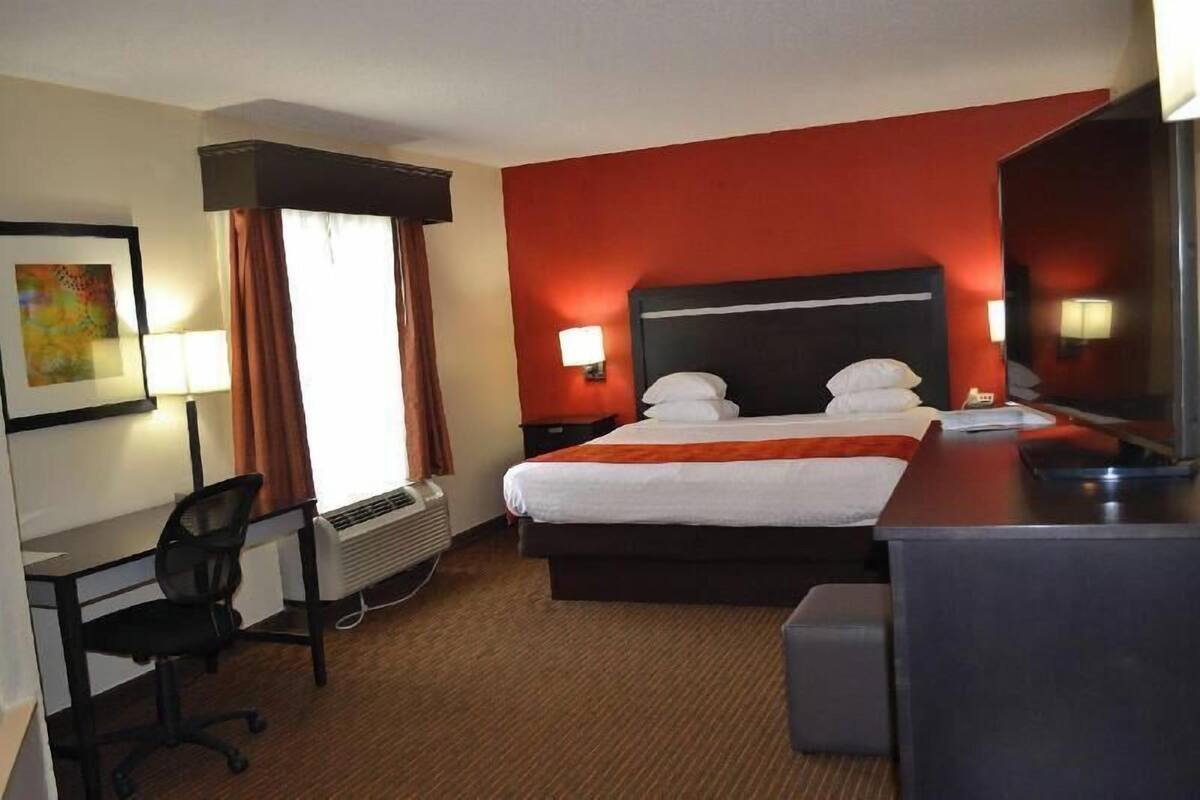 A hotel room with a bed, desk, chair, and a large mirror.