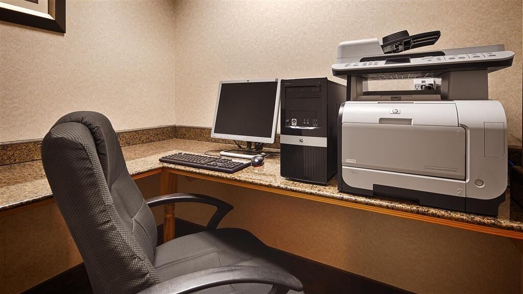 A hotel workspace with a desktop computer, two monitors, a printer, and a chair.