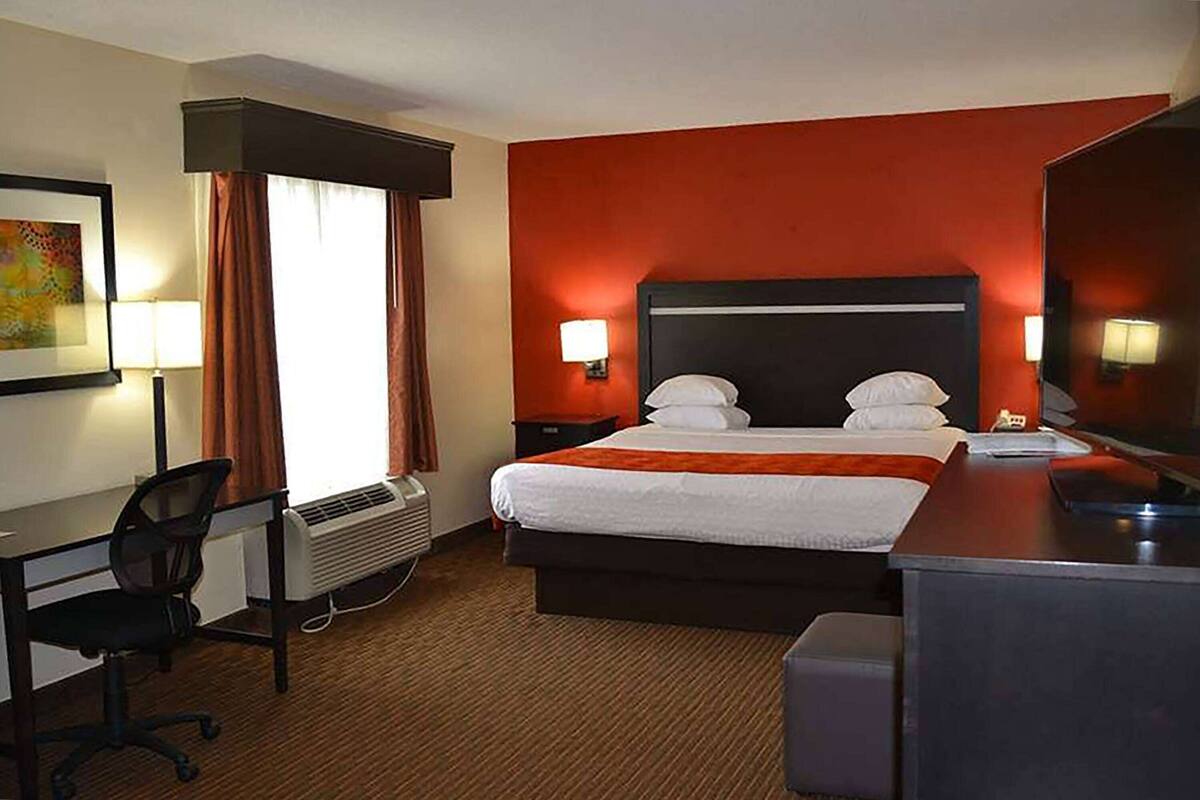 A hotel room with a bed, desk, chair, and a large mirror.