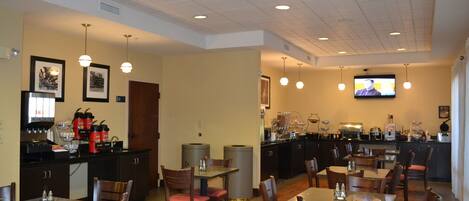 A restaurant with multiple tables and chairs, a kitchen area, and a television mounted on the wall.