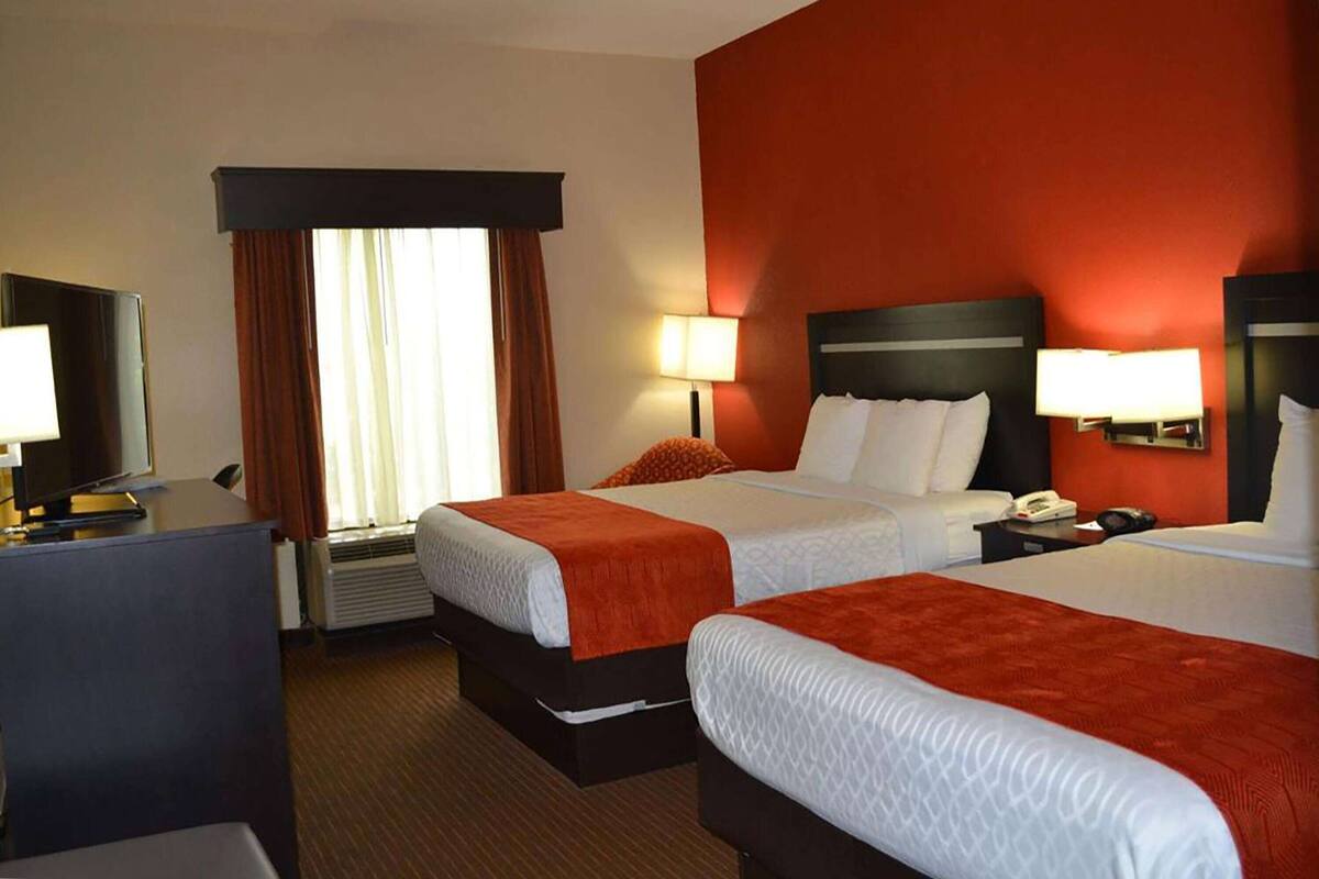 A hotel room with two beds, a desk, a TV, and a window with curtains.