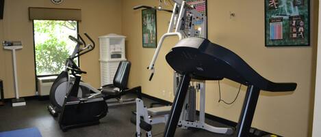 Une salle de sport équipée de divers appareils, notamment un tapis de course, un vélo elliptique et des appareils de musculation.