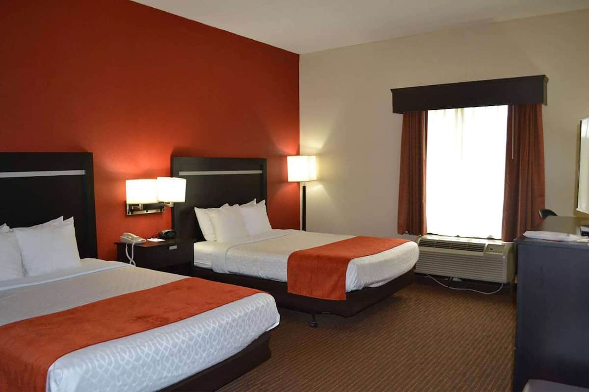 A hotel room with two beds, a desk, a phone, a lamp, an air conditioner, and a window with curtains.