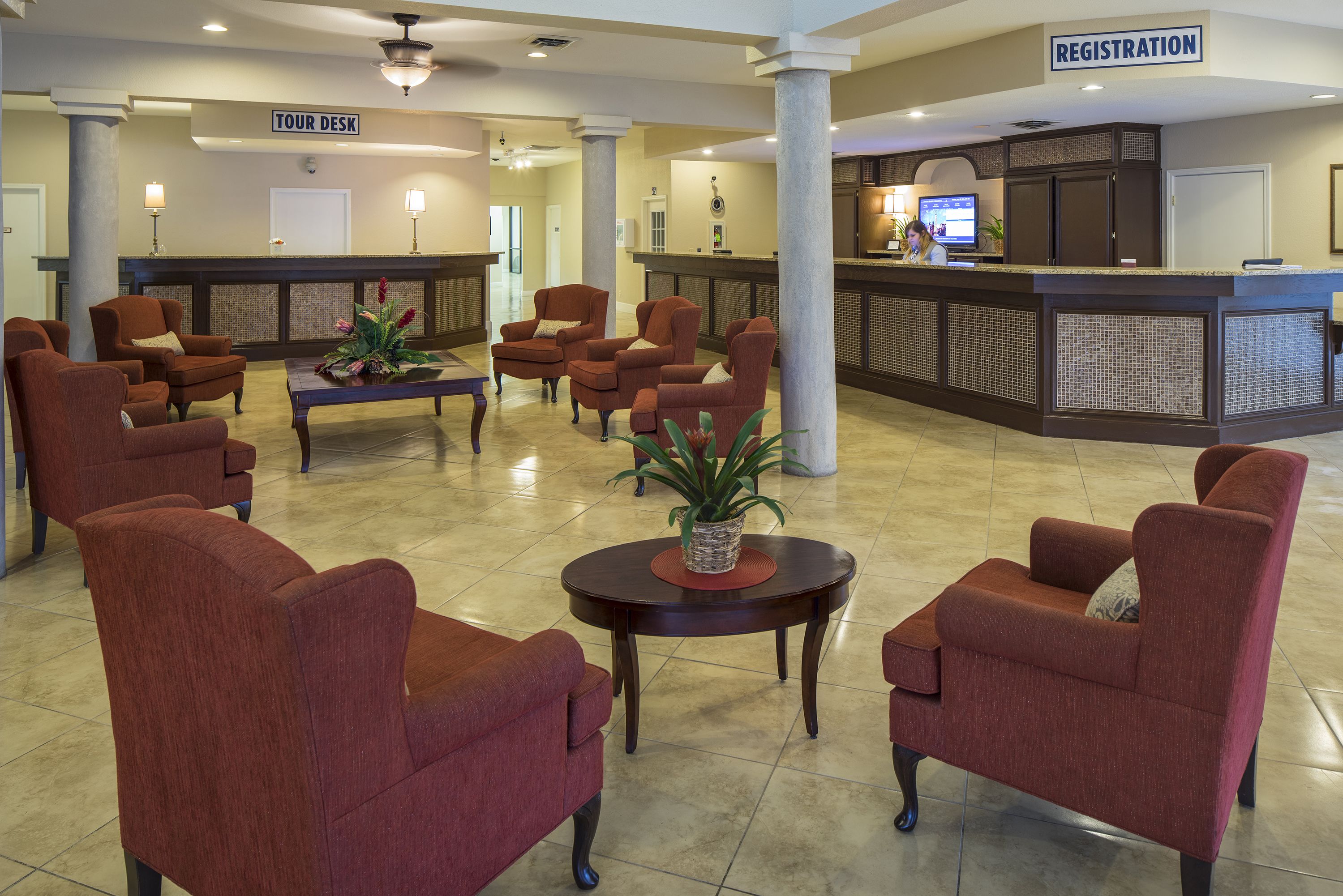 A hotel lobby with a reception desk, registration area, and several armchairs arranged around a central table with a plant.