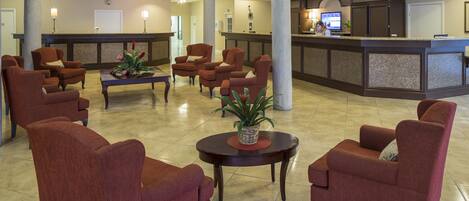 A hotel lobby with a reception desk, registration area, and several armchairs arranged around a central table with a plant.
