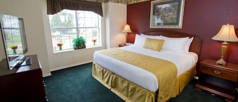 A hotel room with a large bed, two bedside tables with lamps, a ceiling fan, a window with a view, and a dresser.