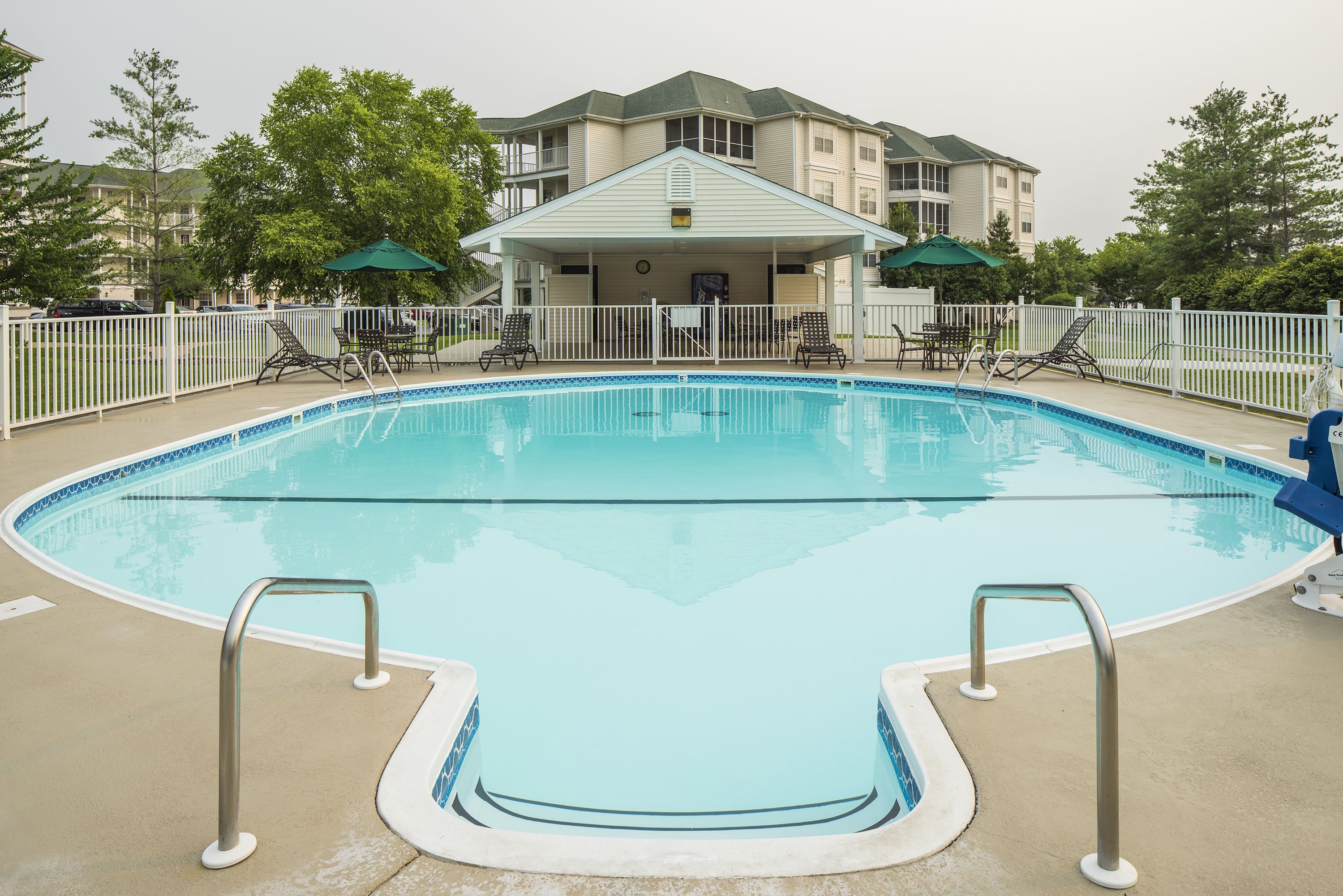 A swimming pool with a covered area and lounge chairs, surrounded by a white fence.