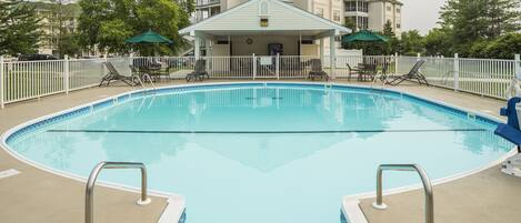 A swimming pool with a covered area and lounge chairs, surrounded by a white fence.