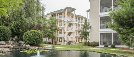 A multi-story residential building with balconies and a pond with a fountain.