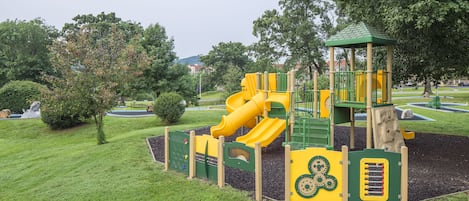 A playground with a yellow slide and green climbing structures.