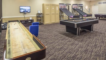 Una mesa de billar, un juego de bolos y un televisor en una sala con casilleros y piso alfombrado.