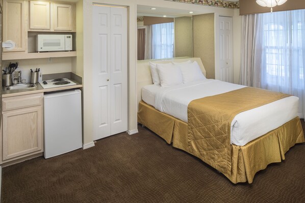 A hotel room with a bed, a microwave, a mini-fridge, and a small kitchenette.