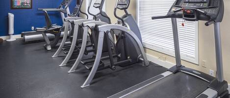 Un gimnasio con cintas de correr, elípticas y una bicicleta estática.