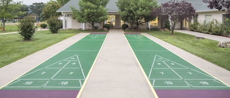 A courtyard with a shuffleboard court, a building with a porch, and trees.
