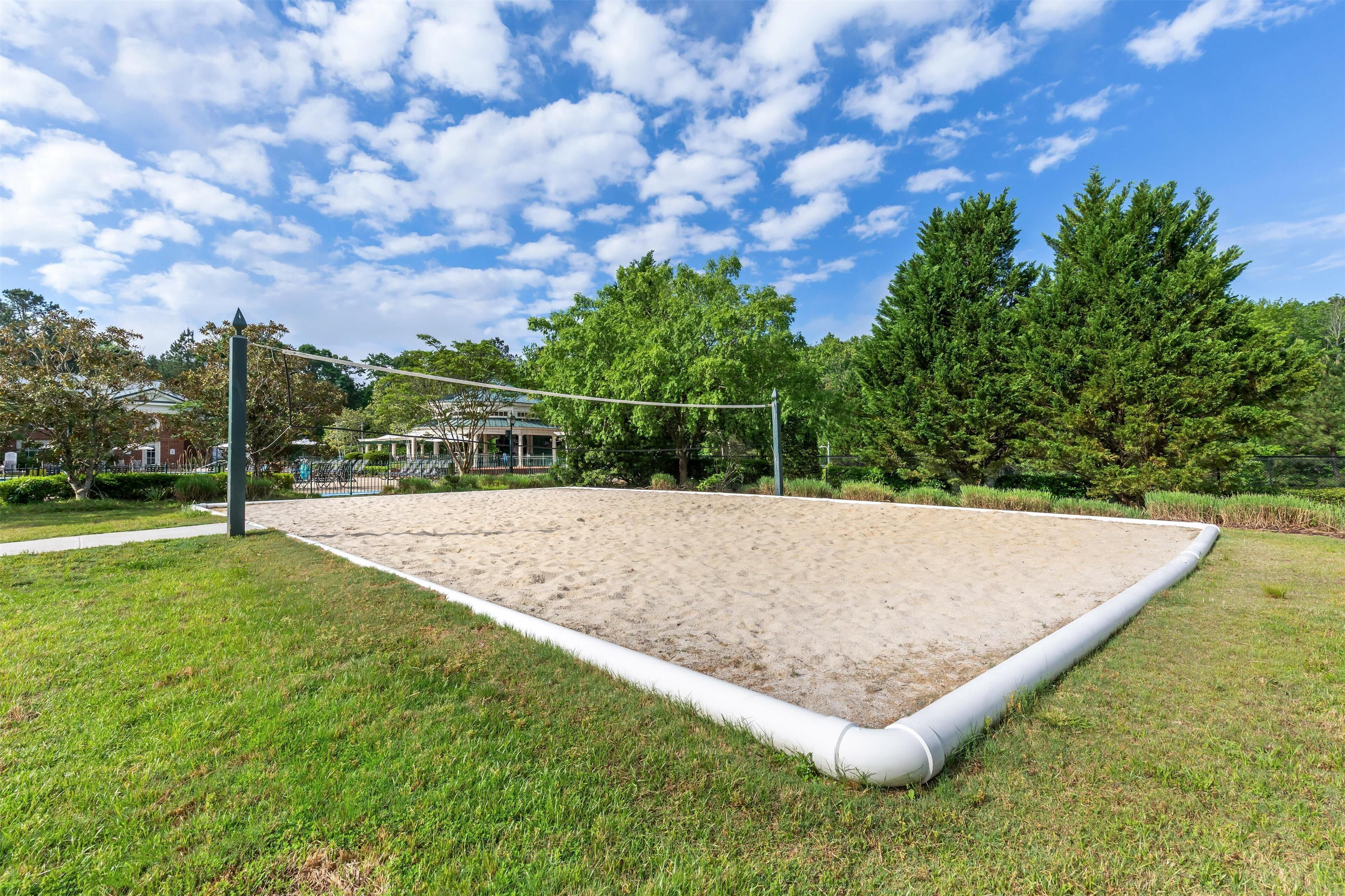 A volleyball court with a net, surrounded by grass and trees.