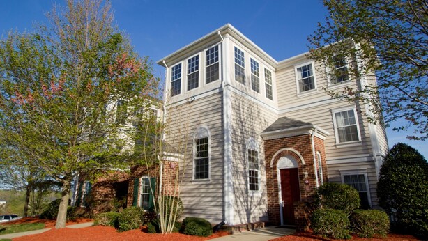 A two-story house with a brick facade and white siding, featuring a prominent front entrance and a small porch.
