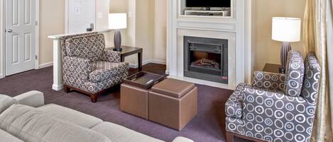 Habitación de hotel con sofá, sillón, reposapiés, chimenea, televisor y lámpara.
