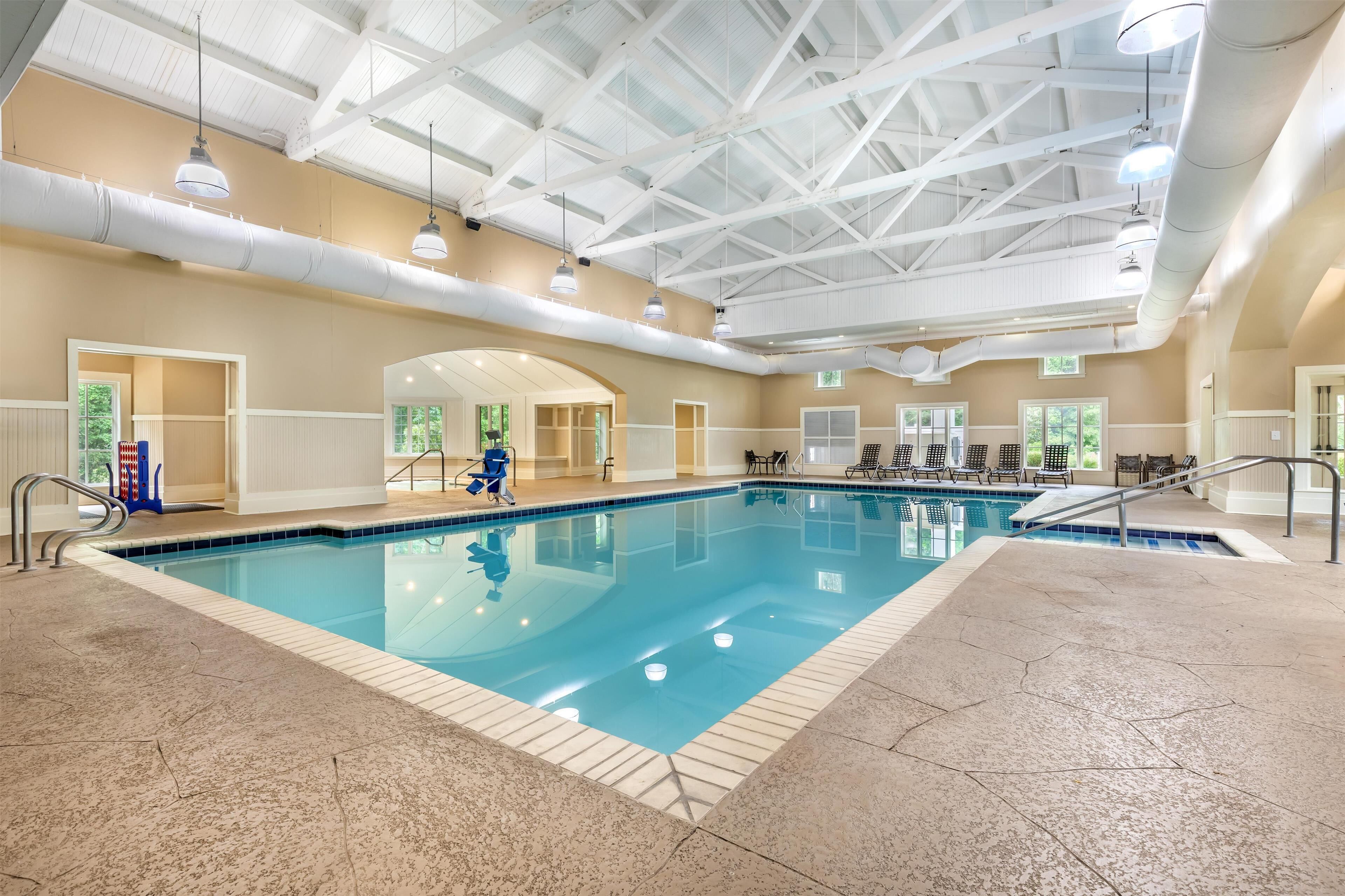 An indoor swimming pool with a high ceiling, large windows, and multiple seating areas.