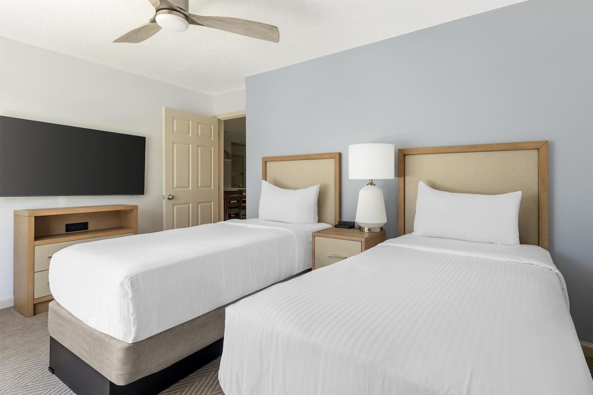A hotel room with two beds, a TV, a ceiling fan, and a door leading to a bathroom.