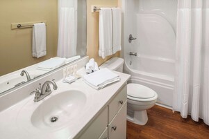 Un baño con lavamanos, inodoro y bañera blancos. Hay toallas en la pared y un espejo sobre el lavamanos.