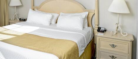 A neatly made bed with a headboard, two bedside tables with lamps, a painting on the wall, and a blue carpet.