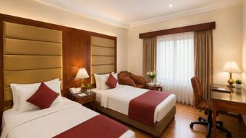 A hotel room with two beds, a desk, a chair, a lamp, and a window with curtains.