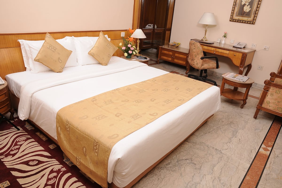 Quarto de hotel com cama, escrivaninha, cadeira e mesinha.
