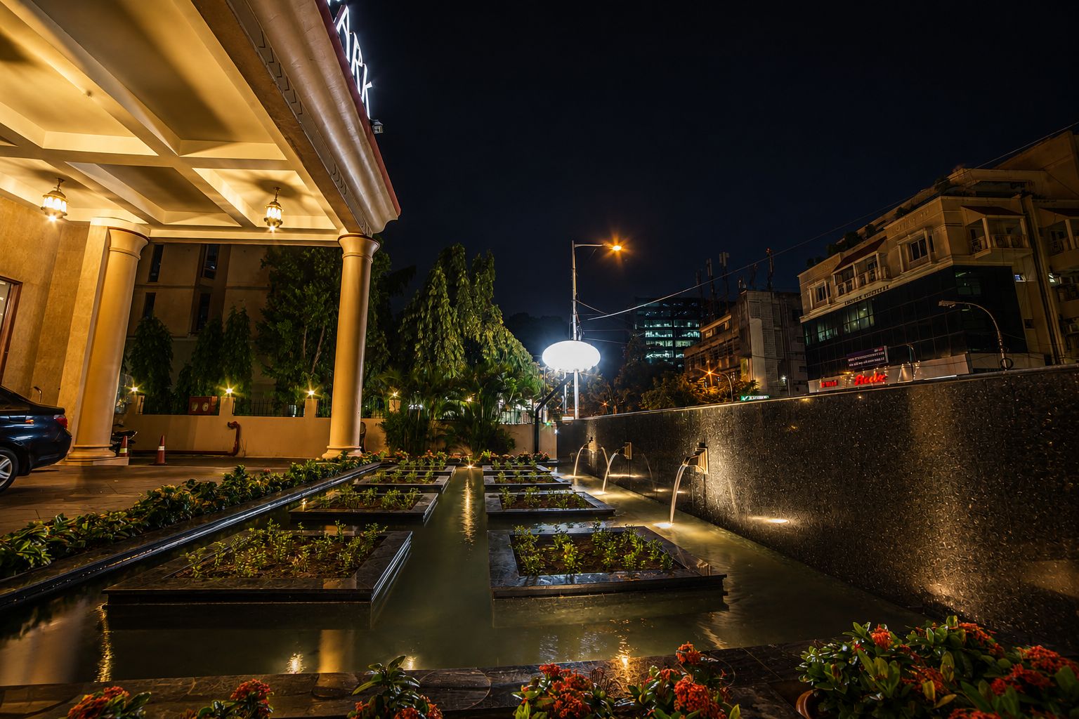 A hotel courtyard at night with a water feature, columns, and a street view.