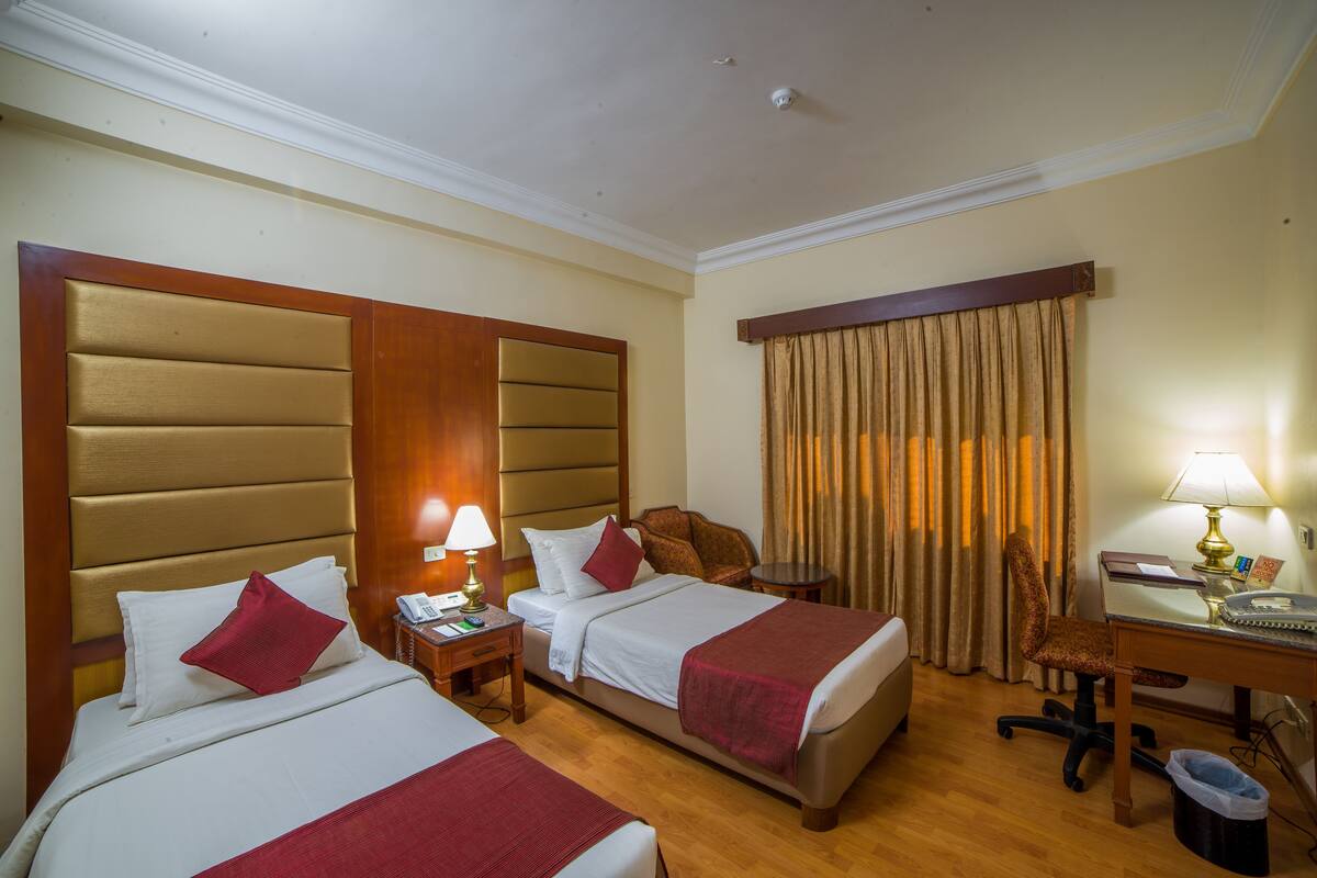 Quarto de hotel com duas camas, uma escrivaninha, uma cadeira, um telefone e uma lixeira.