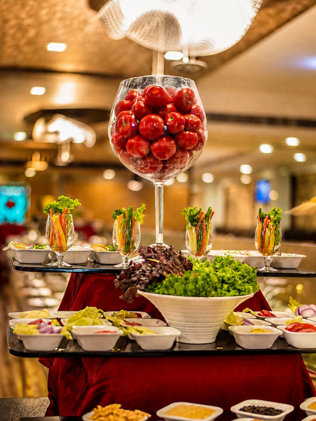 A buffet table with various food items, including a glass filled with cherry tomatoes, bowls of salad, and other dishes.