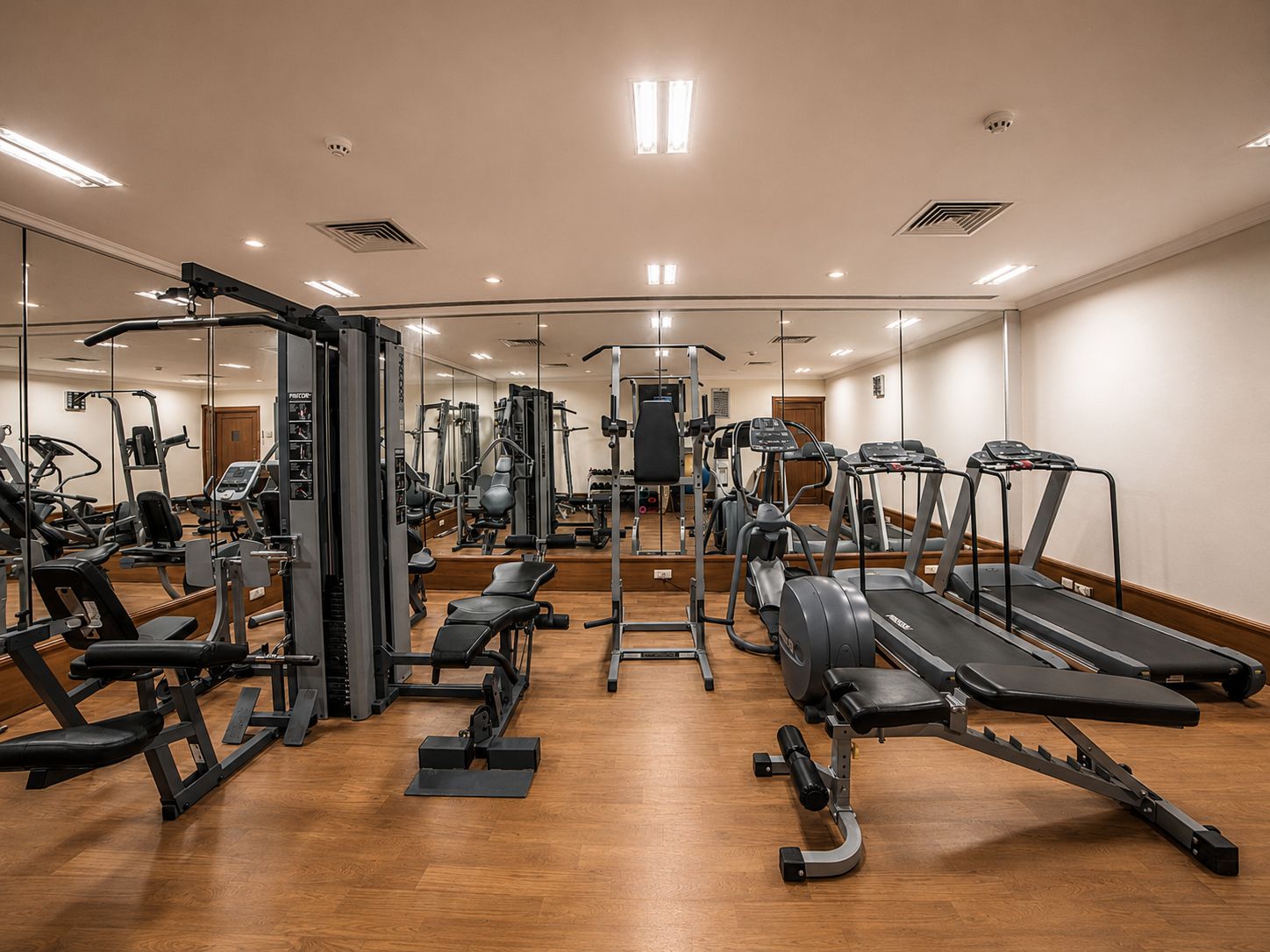 Ein Fitnessstudio mit unterschiedlichen Trainingsgeräten, darunter Laufbänder und Kraftgeräte, sowie einer Spiegelwand.