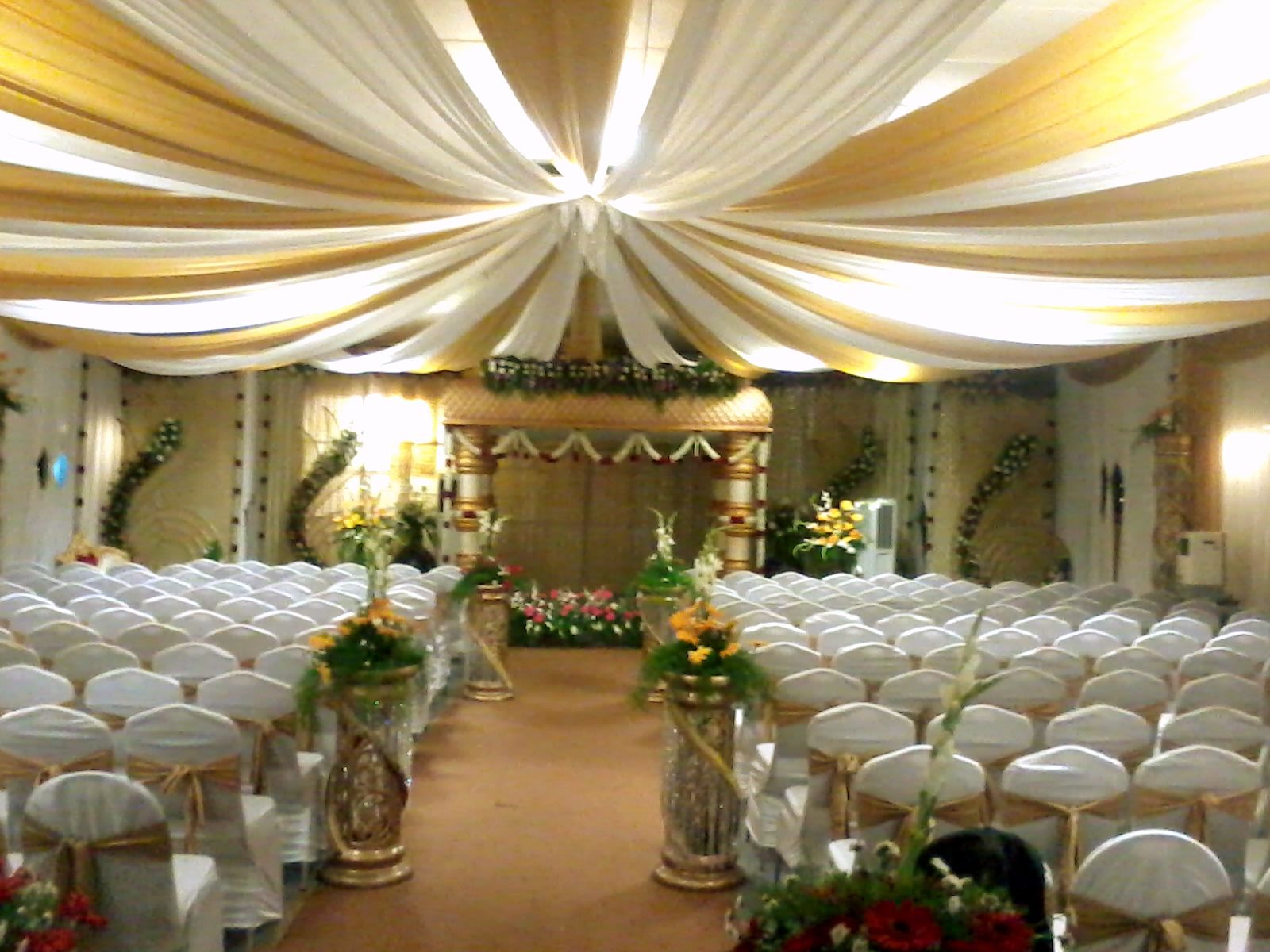 A church interior with rows of white chairs, a central aisle, and floral decorations.