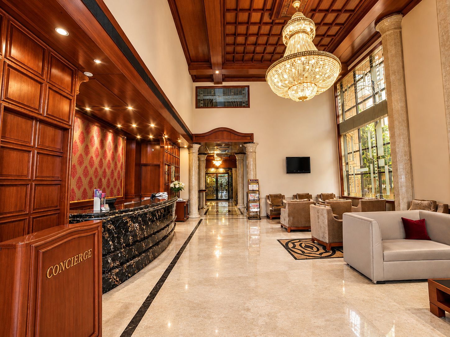 A hotel lobby with a reception desk, seating area, and a chandelier.
