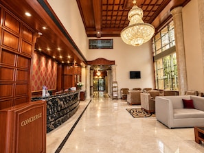 A hotel lobby with a reception desk, seating area, and a chandelier.