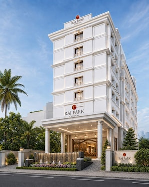 Un hotel de varios pisos con una entrada destacada, palmeras y cielo despejado.