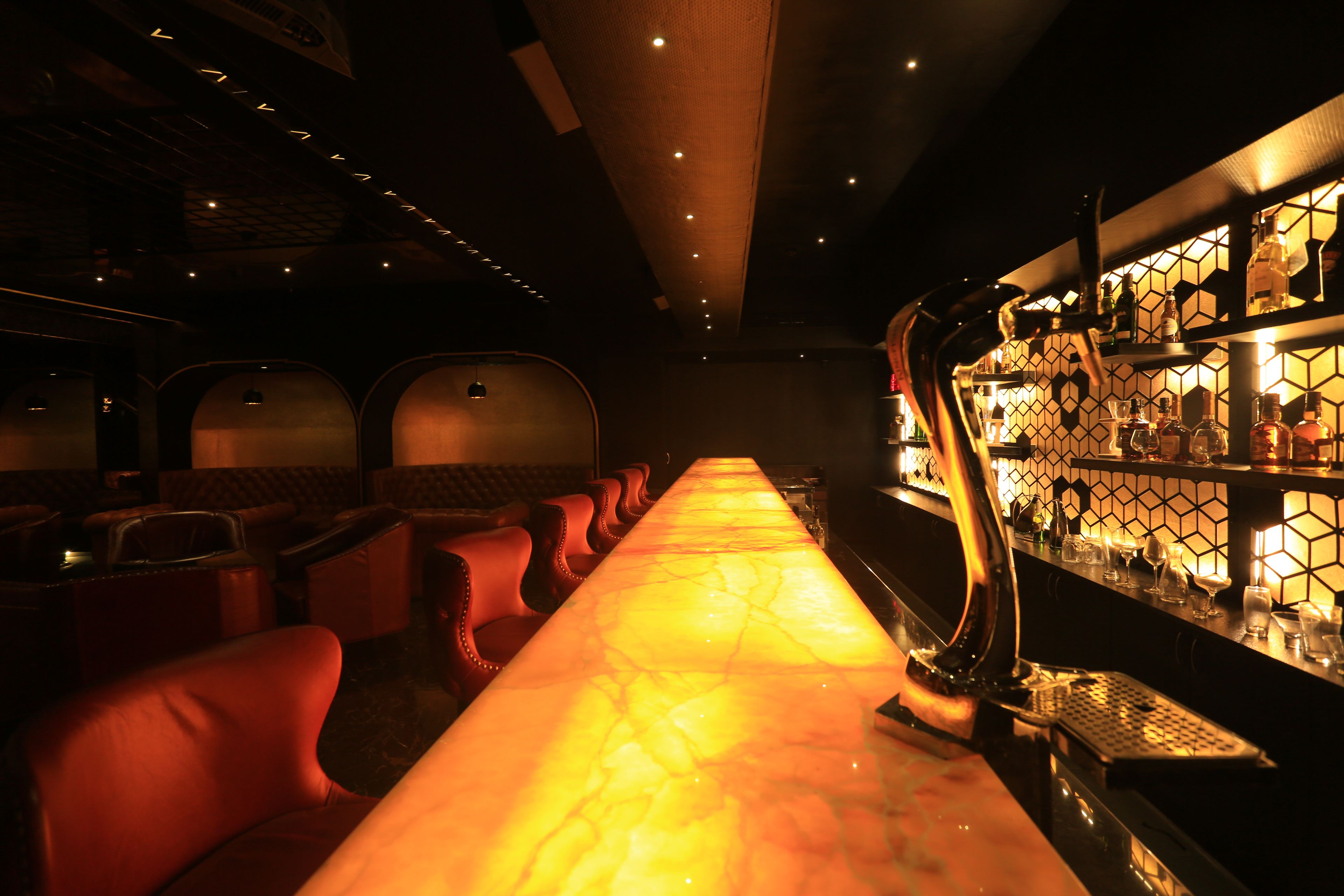 A bar area with a long counter, bar stools, and a well-lit bar stocked with bottles.