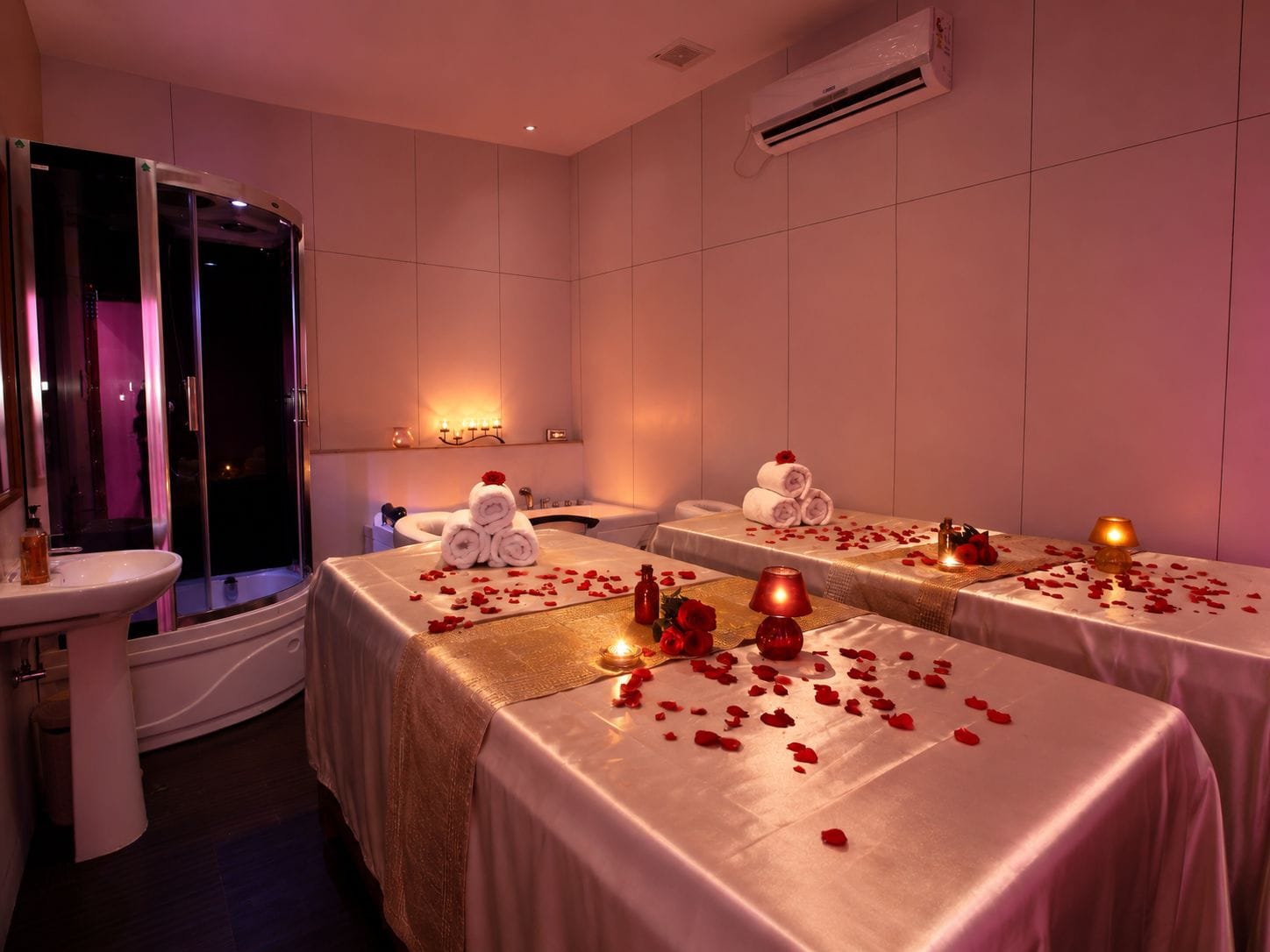 A hotel room with a shower, two beds, a vanity, and a massage table.