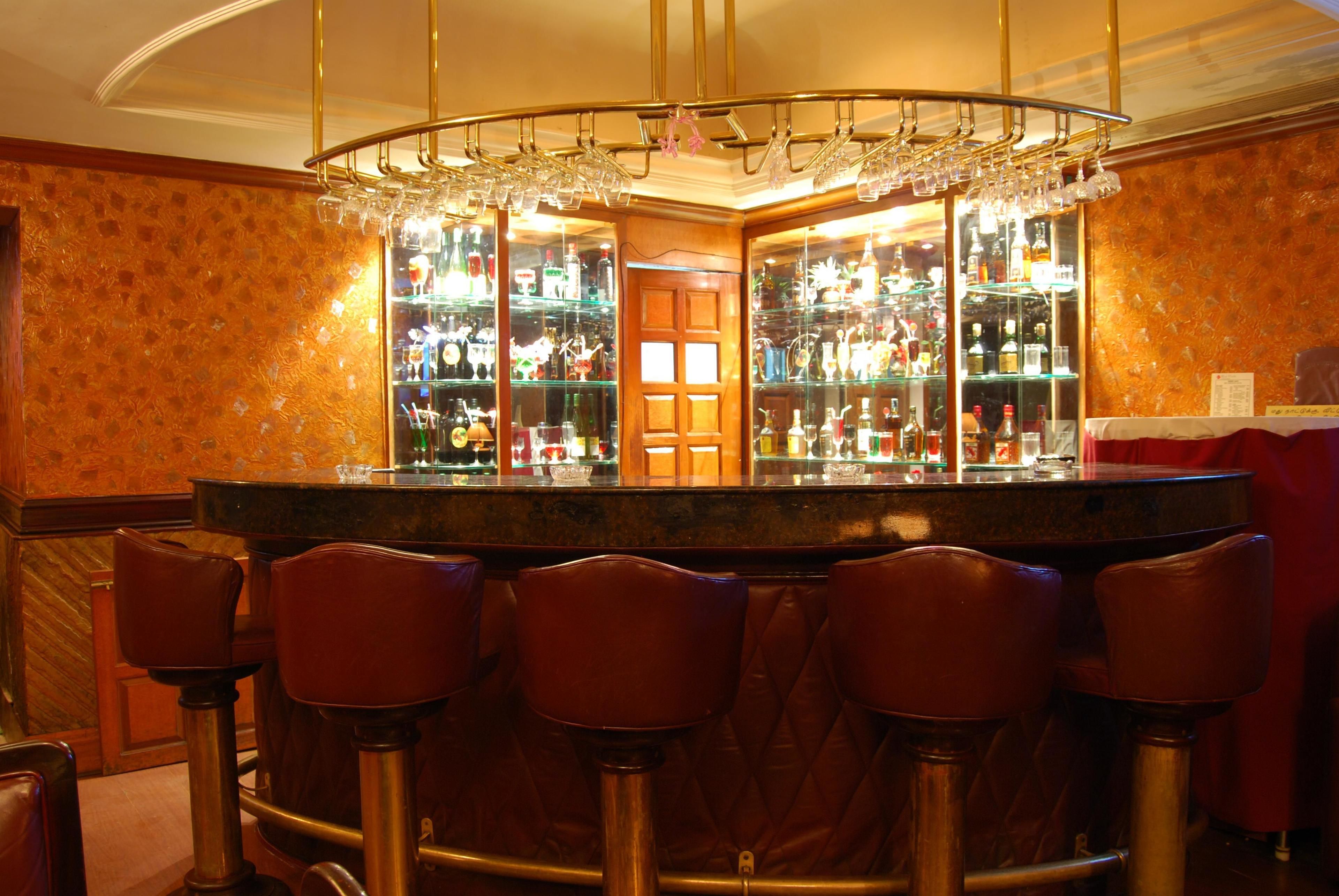 Een bar met een rond aanrecht, verschillende krukken en een glazen vitrine vol flessen.