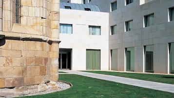 Un edificio moderno con una columna de piedra, un camino empedrado y una zona verde.
