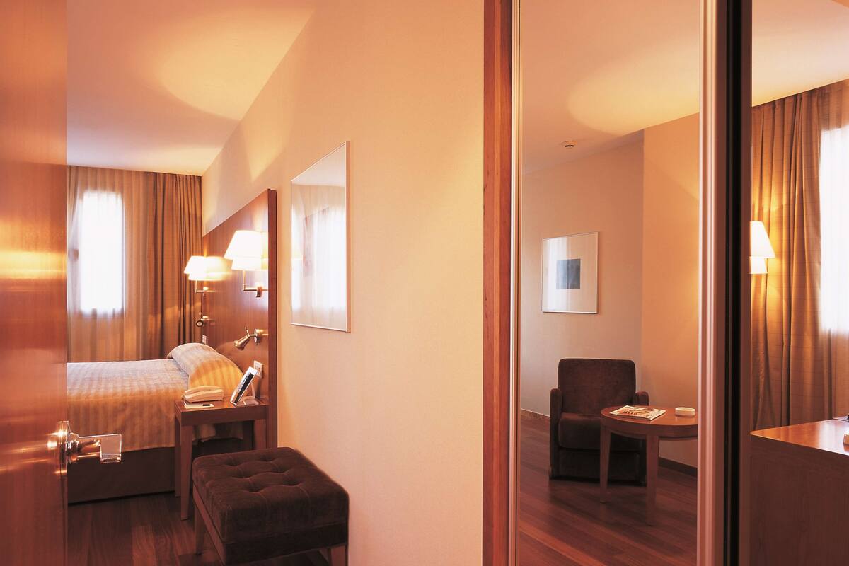 A hotel room with a bed, a desk, a chair, and a mirror.