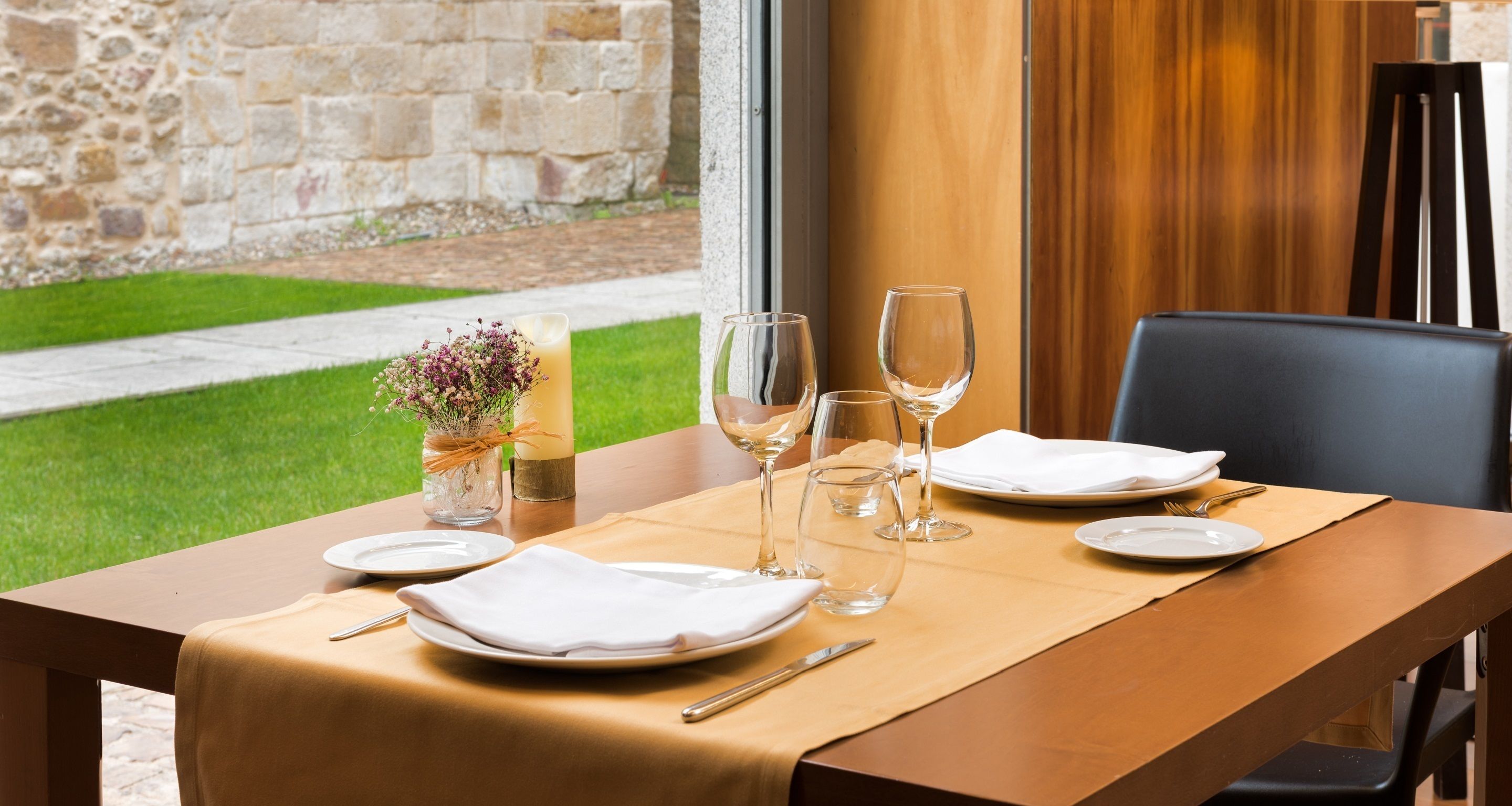 A dining table set with plates, cutlery, and wine glasses, with a candle and flowers on the table.