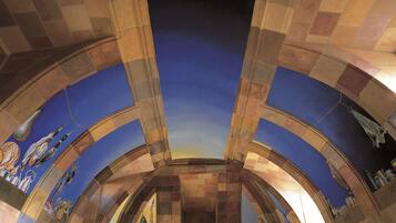 A room with a vaulted ceiling, a mural with birds and fruits, and a view of the sky through a circular opening.