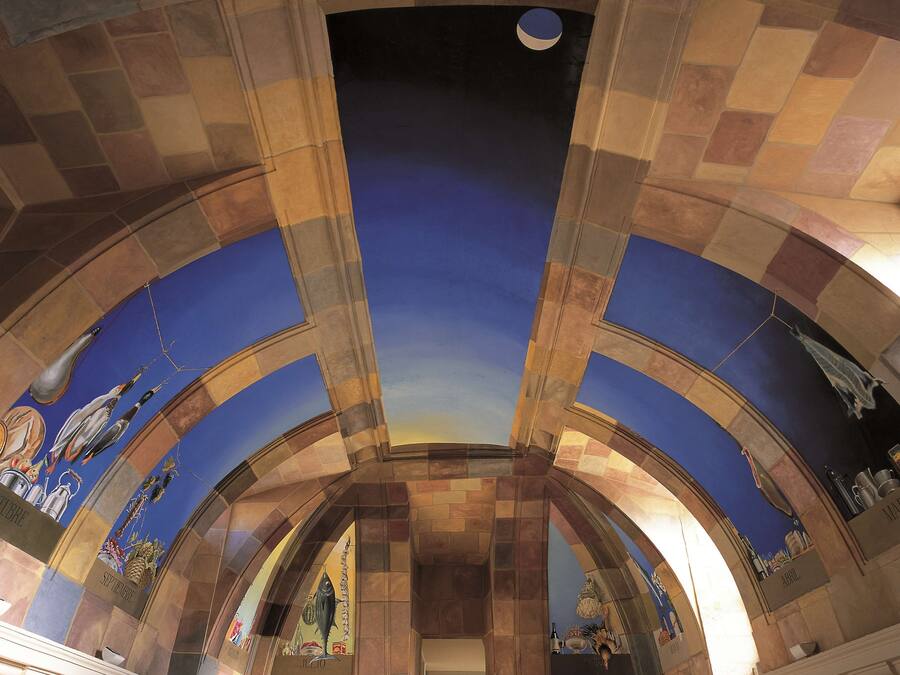 A room with a vaulted ceiling, a mural with birds and fruits, and a view of the sky through a circular opening.