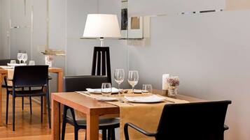 Un comedor con una mesa de madera dispuesta para dos comensales, sillas negras, una lámpara de mesa y un florero con flores.