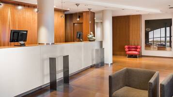 A modern reception area with a wooden reception desk, a flat-screen TV, and a red chair.