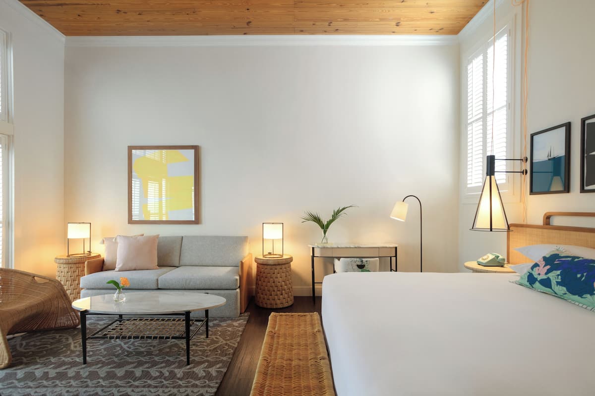 A hotel room with a bed, a sofa, a coffee table, a lamp, and a small side table.