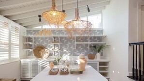A bright kitchen with white cabinetry, a white island, wicker pendant lights, and geometric patterned backsplash. - Ella's Cottages - Key West Historic Inns (Key West)